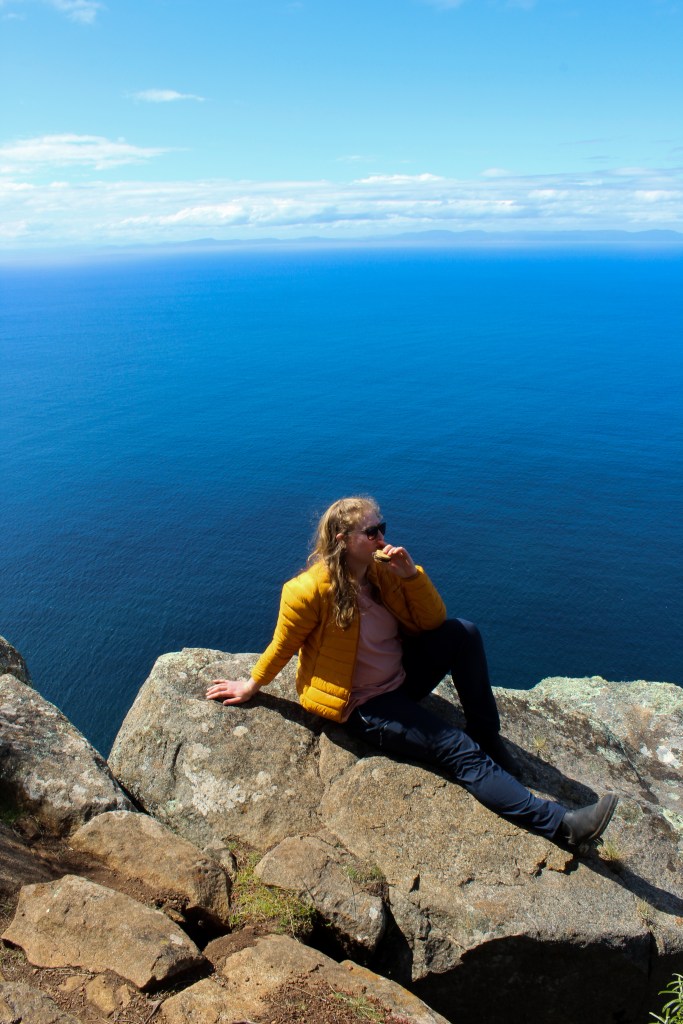 Sapphire lounges on a rock eating a biscuit, overlooking the ocean far below.
