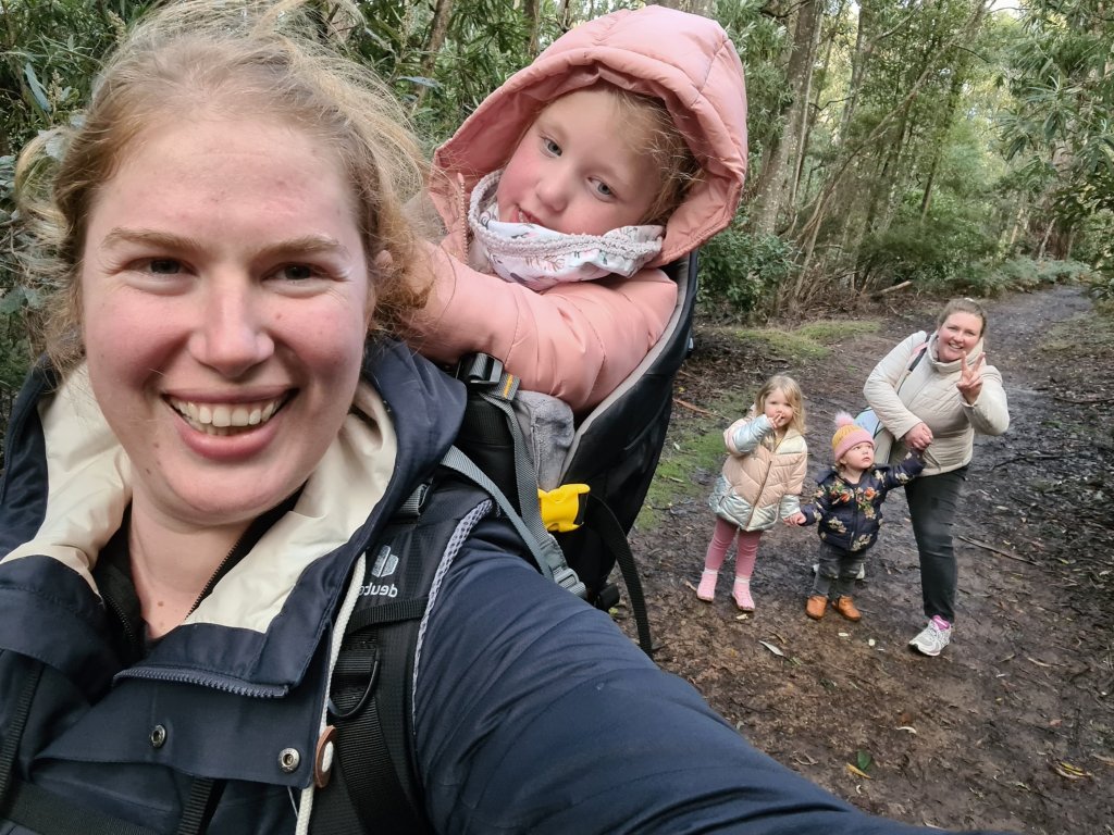 Sapphire, with Miss 4yo on her back stand in the foreground of a selfie with Miss 3yo, Miss under 2yo and Mummy L in the background all holding hands. Mummy L is making a peace sign with her fingers.