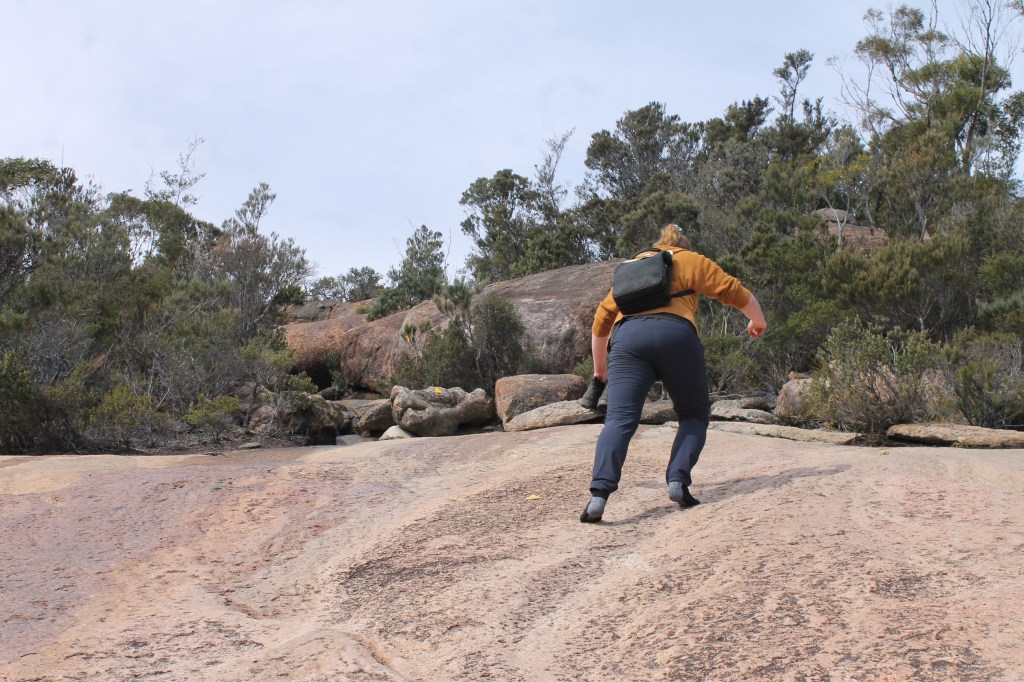 Sapphire is viewed from behind wearing black socks with grey heels and carrying her boots in her hands.