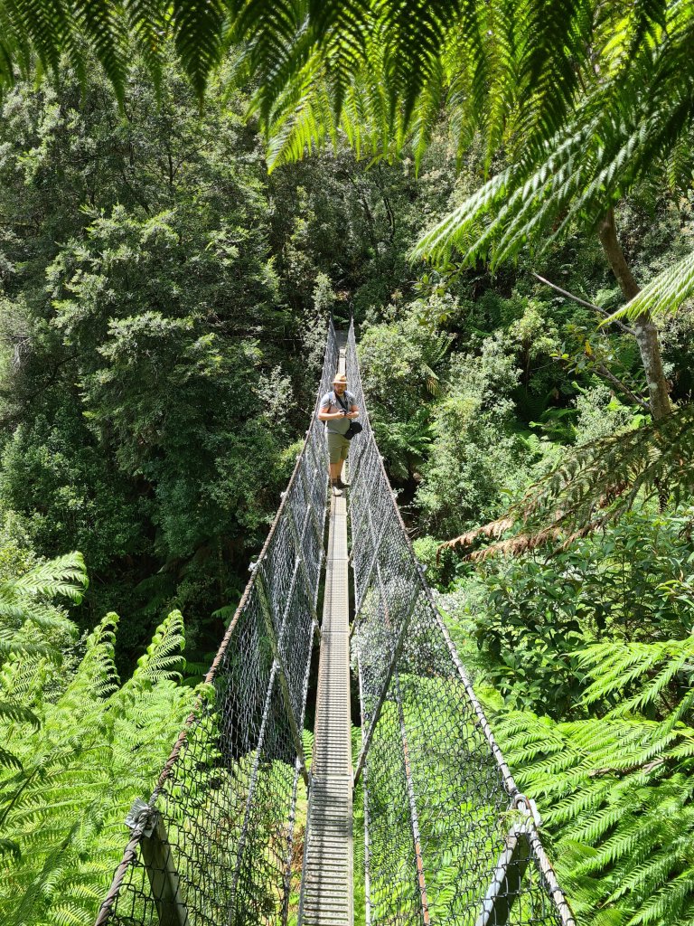 Sommelier, in beige clothes, carrying his camera stops on the suspension bridge to admire the falls (which aren't visible in this picture) 
