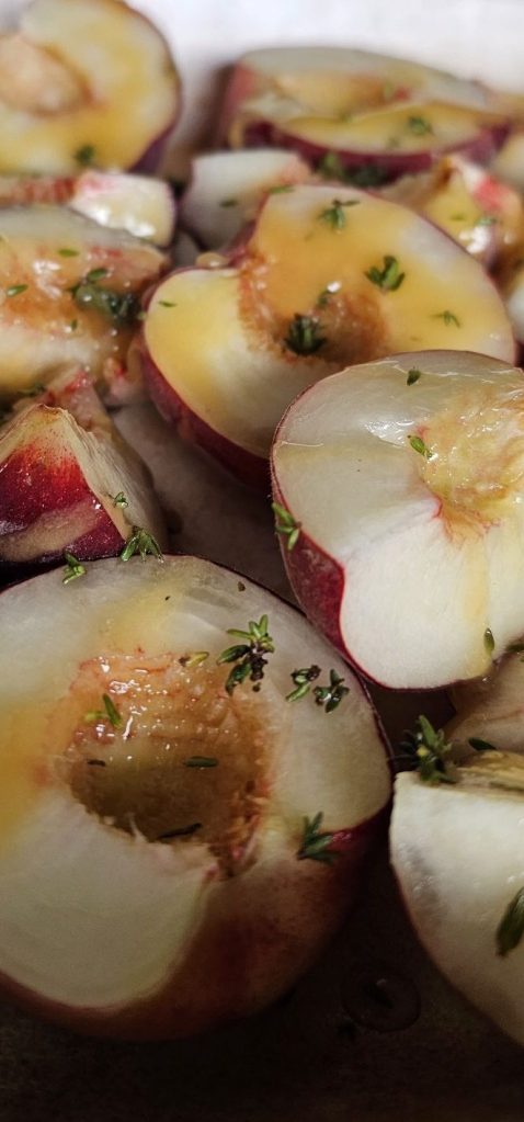 peaches sprinkled with thyme leaves and honey wait to go into the oven. 